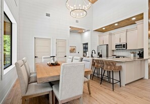 Een moderne keuken met witte kasten, een houten kookeiland met barstoelen, en een eethoek met een houten tafel en stoelen.