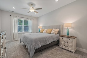 A bedroom with a bed, bedside lamps, a dresser, a ceiling fan, and a window with curtains. - Stunning&Serene Golf Resort Condo (Calabash)