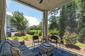 A covered patio with a sofa, chairs, and a small table, overlooking a landscaped garden and residential buildings. - Stunning&Serene Golf Resort Condo (Calabash)