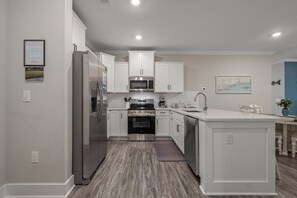 A modern kitchen with white cabinetry, stainless steel appliances, and a central island with seating. - Stunning&Serene Golf Resort Condo (Calabash)