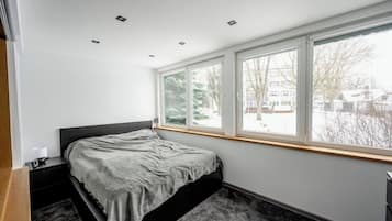 A bedroom with a bed, bedside table, and a window with a view of a snowy landscape.