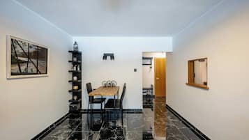 A dining area with a table and chairs, a black marble floor, a wall-mounted shelf with decorative items, and a painting.