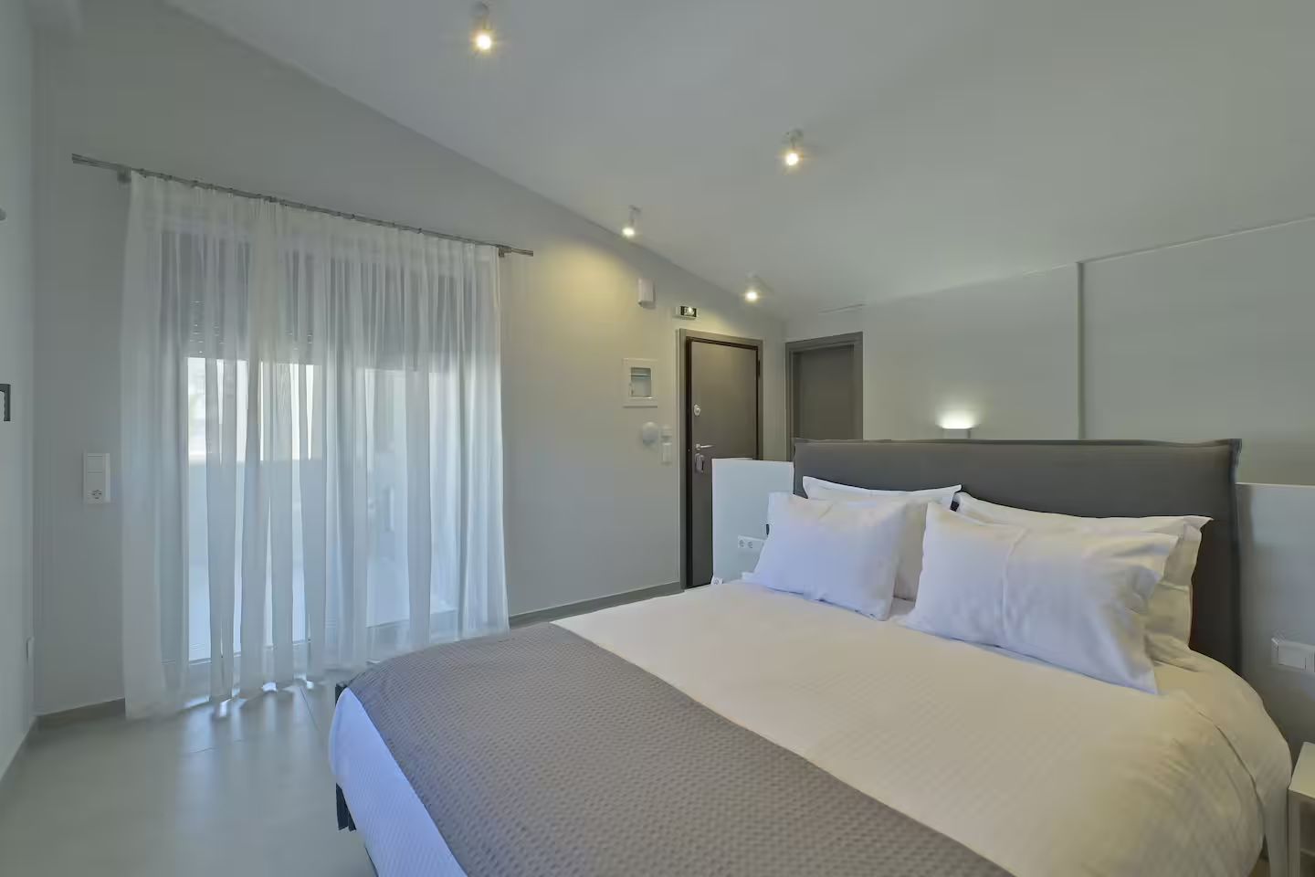 A modern hotel room with a large bed, a door, and a window with curtains.