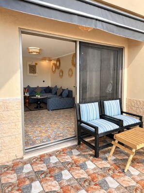 An outdoor seating area with a sofa and chairs, a wooden table, and a patterned floor.