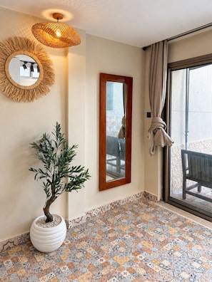 A room with a patterned floor, a potted plant, a mirror, and a window with curtains.