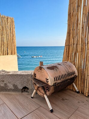 A barbecue grill positioned on a wooden deck with a view of the sea.