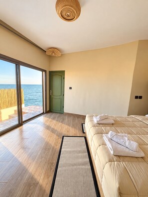 Ein Schlafzimmer mit großem Fenster, einem Bett, einer Tür und Blick aufs Meer.