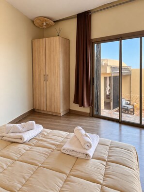A hotel room with a large bed, a wardrobe, and a sliding glass door leading to an outdoor area.