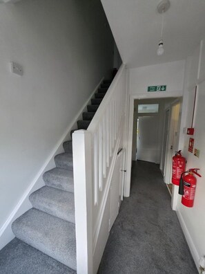 A staircase with a white handrail, carpeted steps, and a fire exit sign above. - Spacious house in Greater London
5 bedrooms 5 bathrooms (London)
