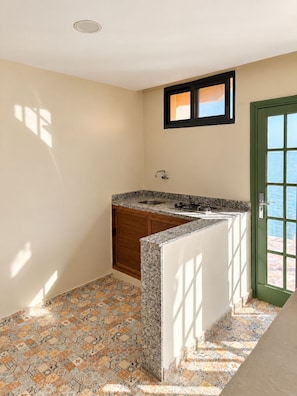 A compact kitchen with a built-in sink, wooden cabinets, and a view of the sea through a green door.