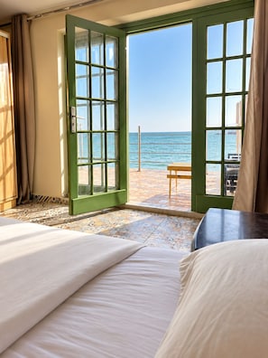 A hotel room with a bed, a table, and a view of the beach.