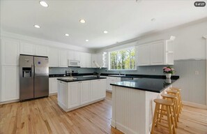 A spacious kitchen with white cabinetry, dual islands, and wood floors. - Hamptons Retreat | Private Pool & 3BR Escape (East Quogue)