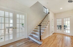 Entry hallway with hardwood floors, staircase, and two sets of French doors. - Hamptons Retreat | Private Pool & 3BR Escape (East Quogue)