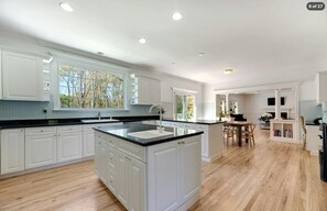 Spacious kitchen with white cabinets, dark counters, and an island leading to the living area. - Hamptons Retreat | Private Pool & 3BR Escape (East Quogue)