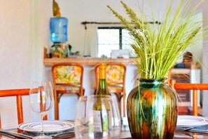 Une table à manger ornée d’un vase de plantes vertes, d’une bouteille de vin et d’un verre.