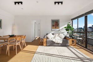 A modern living space with a dining area, a sofa with cushions, a large window with a city view, and a plant. - Sydney Panorama Iconic City Views and Rooftop Pool (Potts Point)