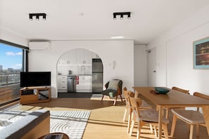 A modern living space with a flat-screen TV, a dining area, and a kitchen with white cabinets. - Sydney Panorama Iconic City Views and Rooftop Pool (Potts Point)