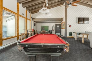 Ein Billardtisch in einem Raum mit hohen Decken, Holzbalken und einem großen Fenster.