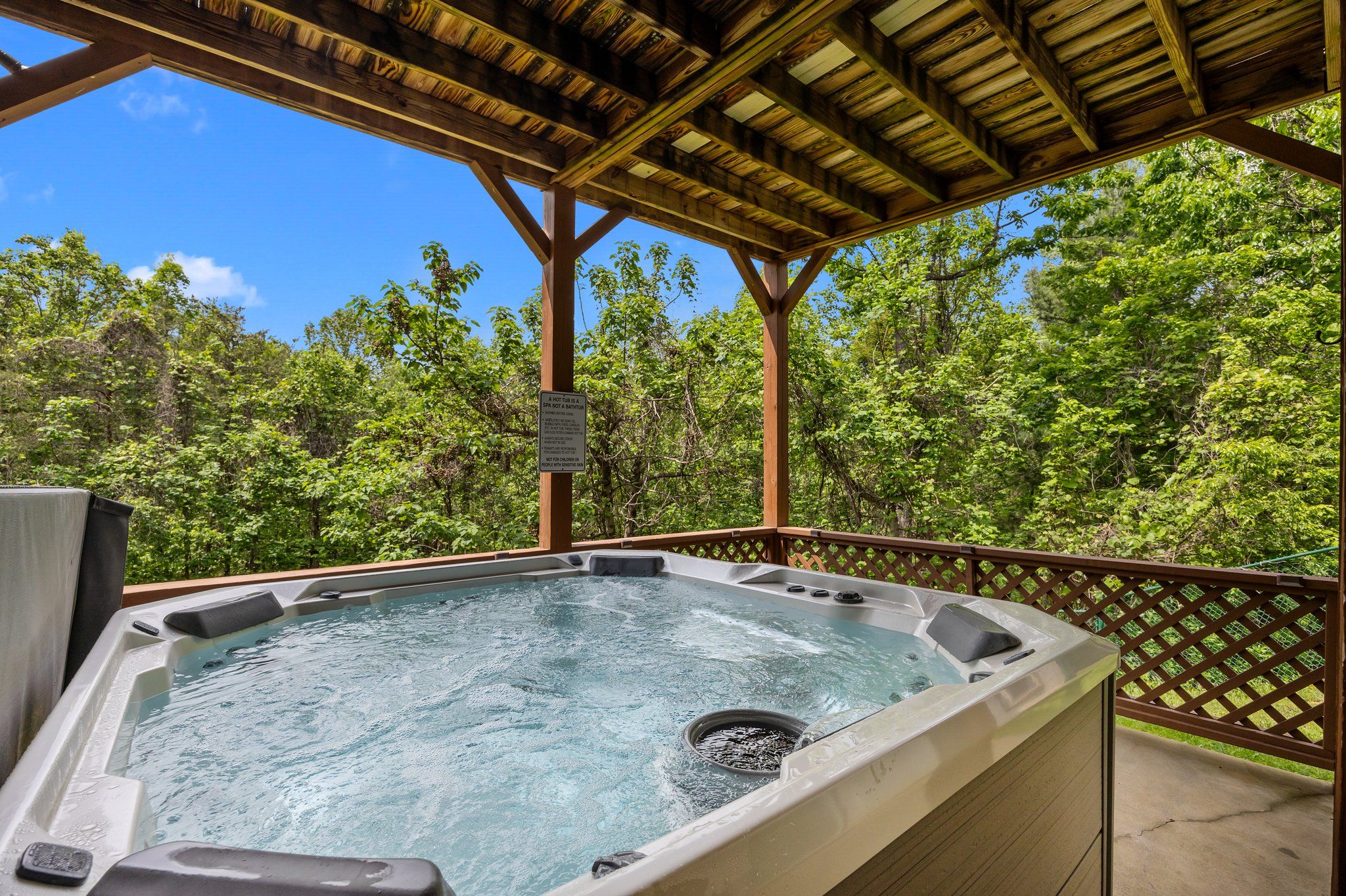 A hot tub under a wooden pergola surrounded by lush greenery.