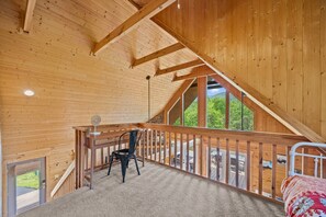 Ein Holzinnenraum mit schrägem Dach, einer Treppe zu einem Balkon und Blick ins Grüne.