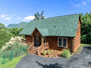 Eine Blockhütte mit grüner Dachdeckung, Holzfassade und einer Veranda mit Stufen zum Eingang.