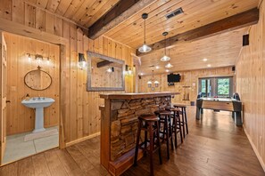 Un intérieur en bois avec un bar en pierre, des tabourets, un évier et une table de billard.