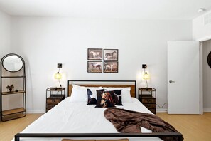A bedroom with a bed, two bedside tables, a round mirror, and wall-mounted artwork. - San Antonio Ranch Loft | 2BR/2BA Garage + Pool (San Antonio)