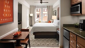 Quarto de hotel com cama, secretária com uma cesta de frutas, micro-ondas e cozinha compacta.