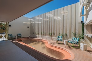 A modern outdoor hot tub area with a curved design, surrounded by lounge chairs and a decorative wall with vertical panels.