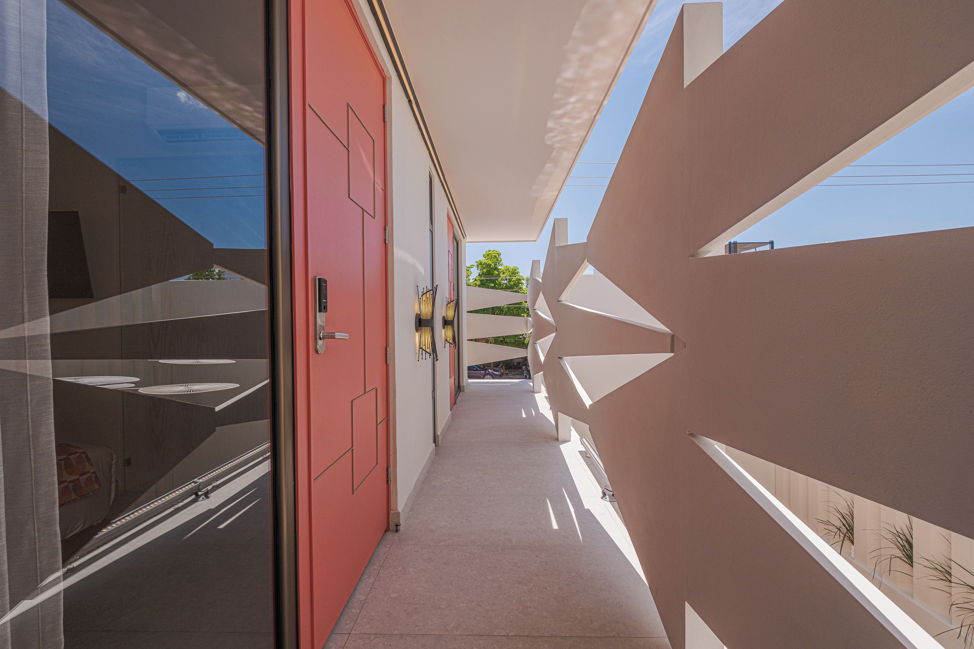A corridor with a red door, a glass wall, and a geometric patterned wall.