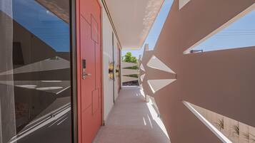 A corridor with a red door, a glass wall, and a geometric patterned wall.