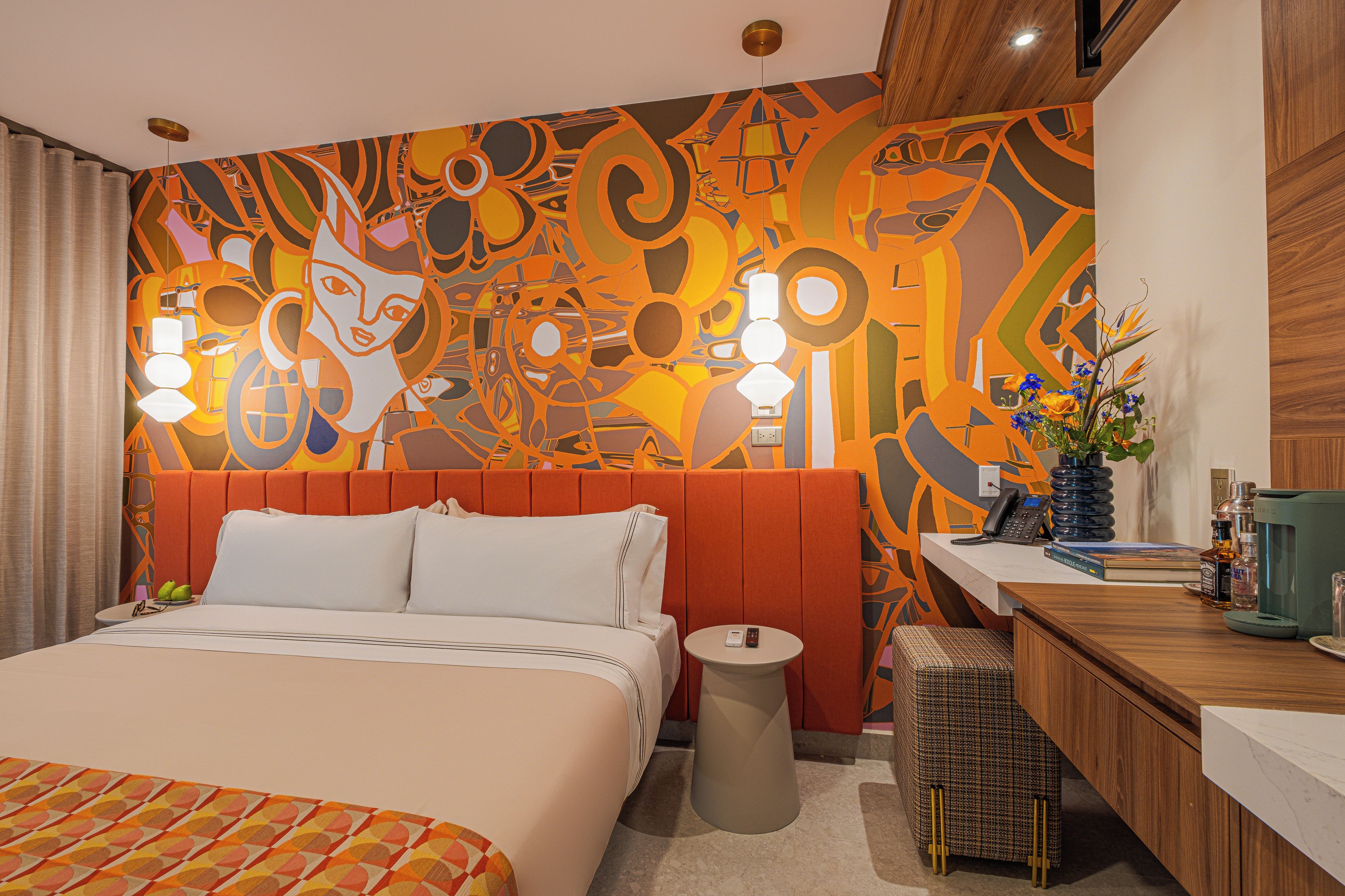 Habitación de hotel con cama, mesita de noche, una pequeña mesa redonda, zona de baño y un detalle decorativo en la pared.