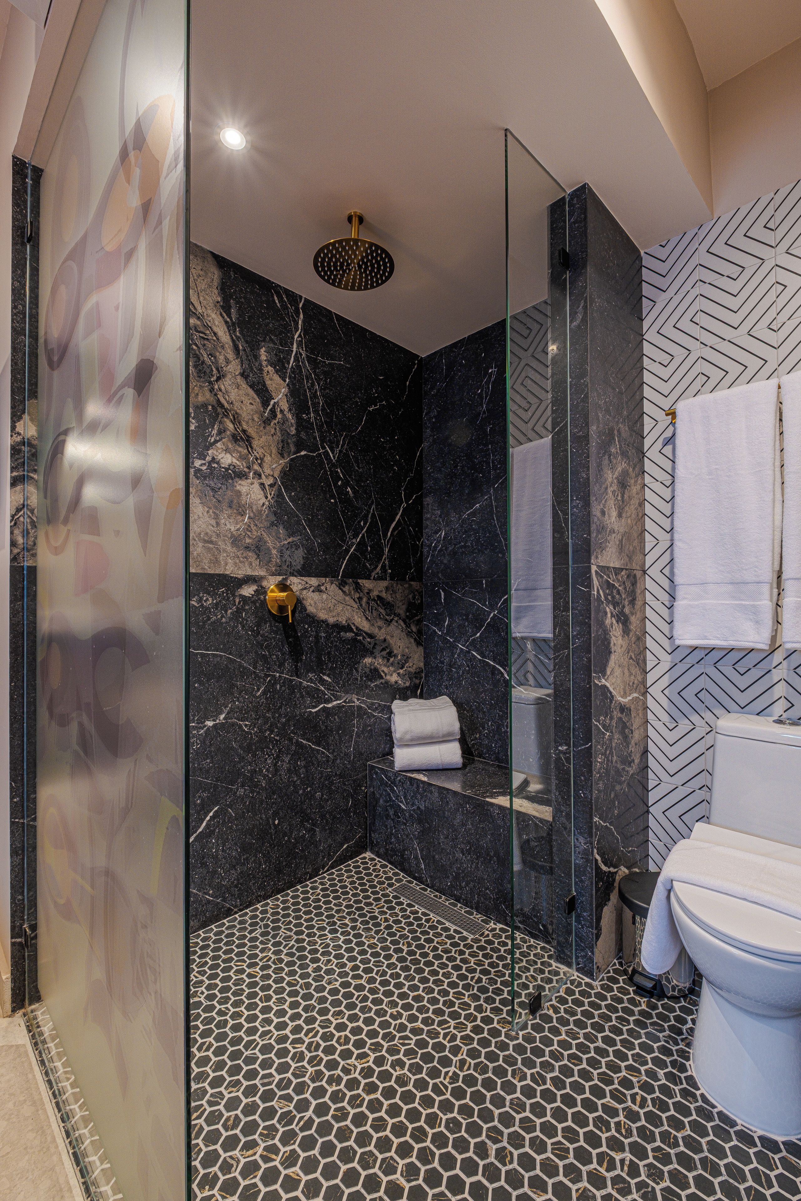 A modern bathroom with a glass-enclosed shower, a marble wall, and a toilet with a patterned floor.
