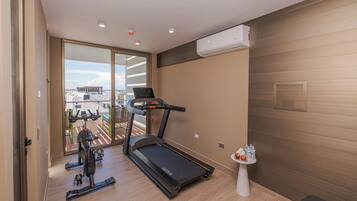 Un gimnasio moderno con cinta de correr, bicicletas estáticas y una pequeña mesa con frutas y botellas de agua.