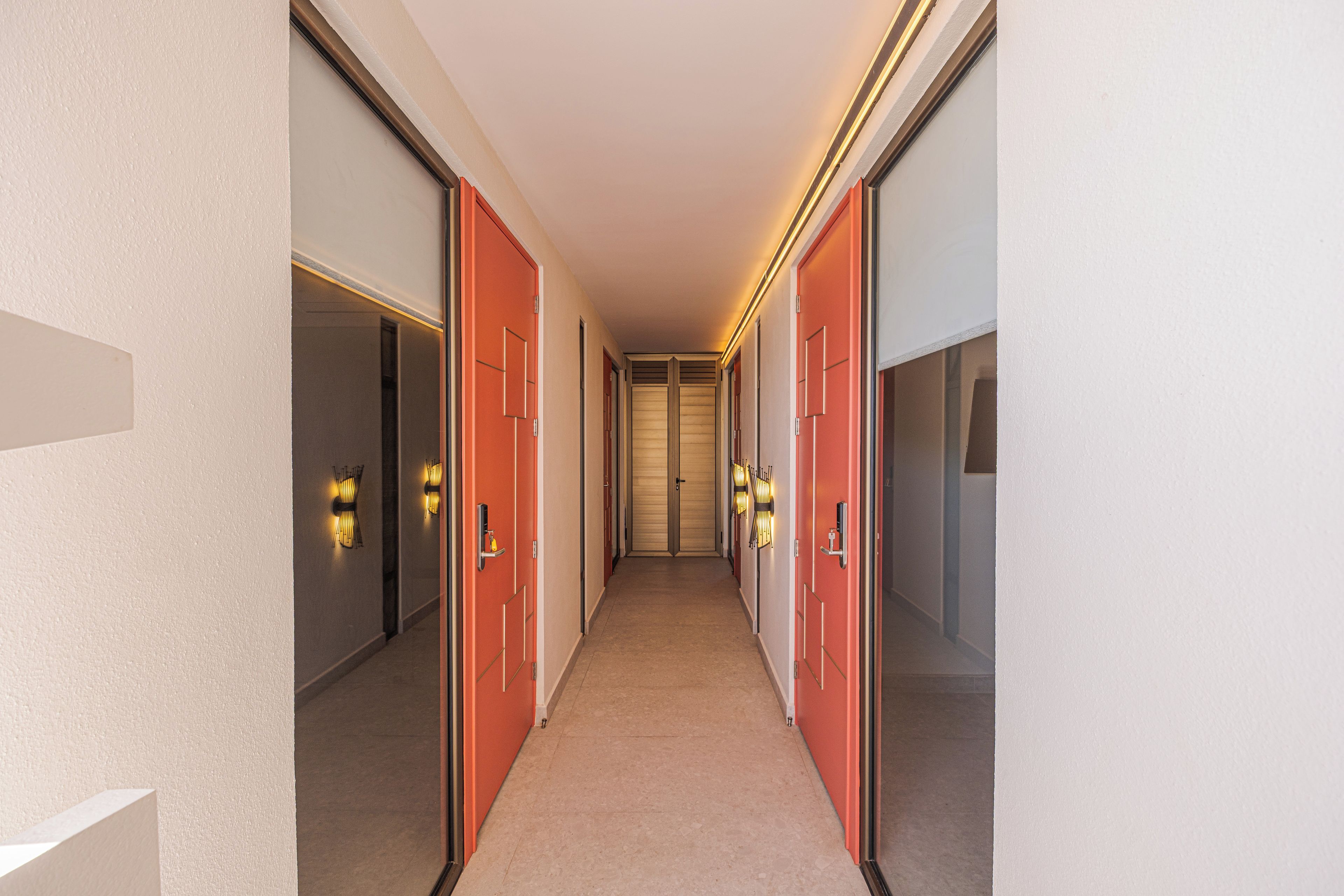 Un pasillo con puertas a ambos lados, piso alfombrado y luces fijadas en la pared.