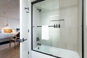 Un bany modern amb dutxa envidrada, una banyera blanca i una taula de nit amb productes de tocador.