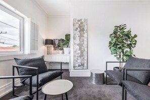 Un salon moderne avec un canapé gris, une petite table ronde, une plante en pot et une grande œuvre d’art abstraite accrochée au mur.