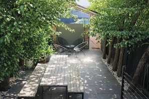 Une terrasse en bois avec une table et des chaises, entourée d’une végétation luxuriante et d’un petit muret.