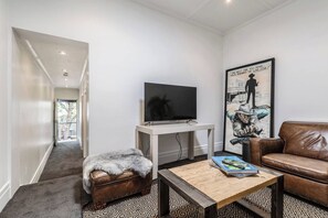 A living room with a television, a sofa, a coffee table, and a framed artwork on the wall. - By the Bay Elegance A Laid back Urban Retreat (Brighton East)