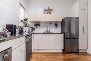 A modern kitchen with white cabinets, a stainless steel refrigerator, and a wooden floor. - By the Bay Elegance A Laid back Urban Retreat (Brighton East)
