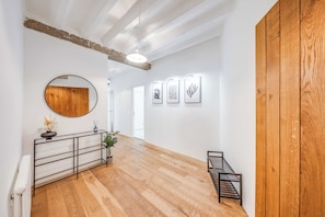 A hallway with wooden flooring, a round mirror, and framed artwork on the wall. - Luxe Penthouse with Balcony & Parking (London)