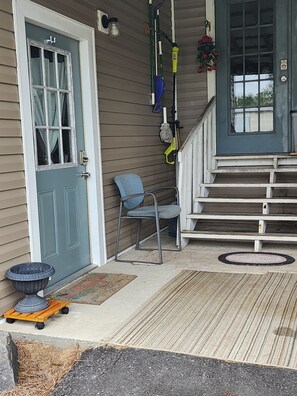 A front porch with a blue door, a blue chair, a set of stairs leading to a dark blue door, and a doormat with 'GENERAL STORE' text.