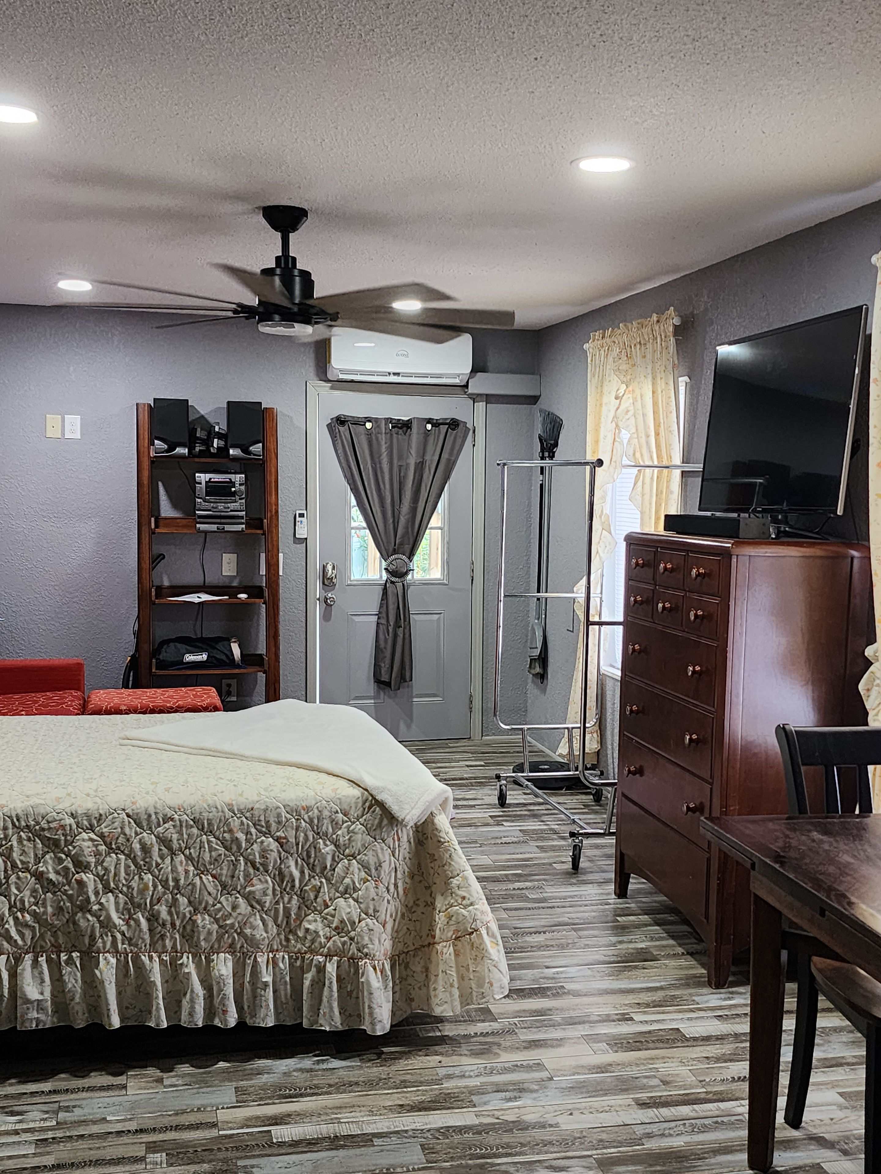 Quarto com cama, cômoda, televisão e ventoinha no teto.