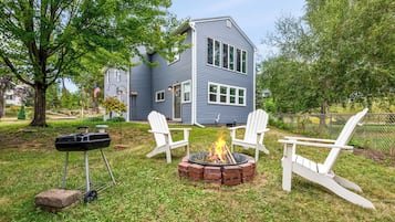 Una casa con un brasero y dos sillas Adirondack en el jardín.