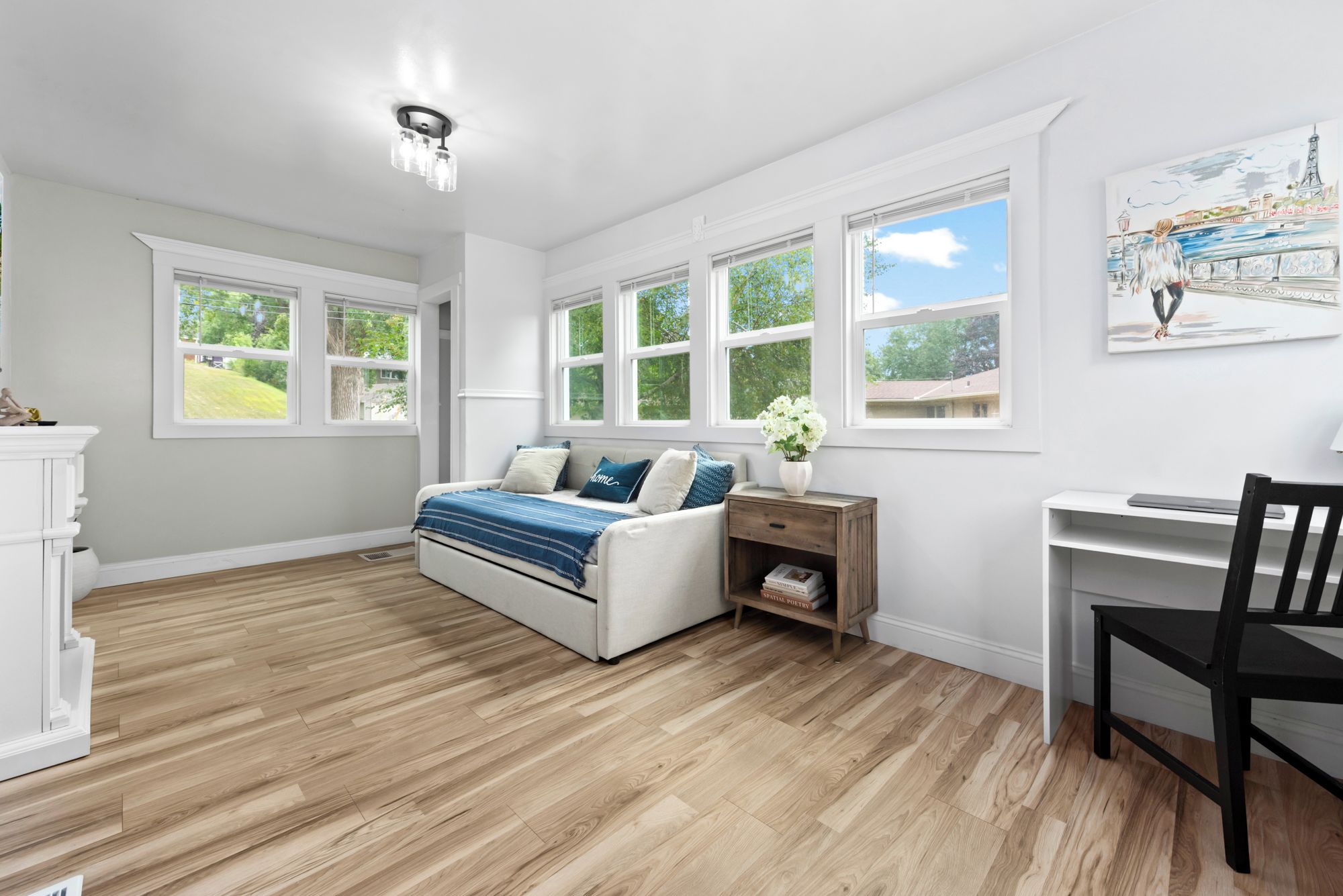 Un dormitorio con cama, escritorio y silla. Ventanas ofrecen vista a zonas verdes.