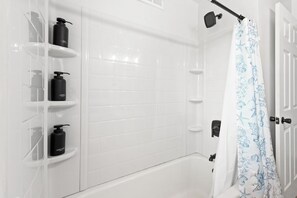 Ein Badezimmer mit weißen Fliesen, einer Badewanne, einer Dusche mit Handbrause und einem Vorhang mit Meeresmotiv.