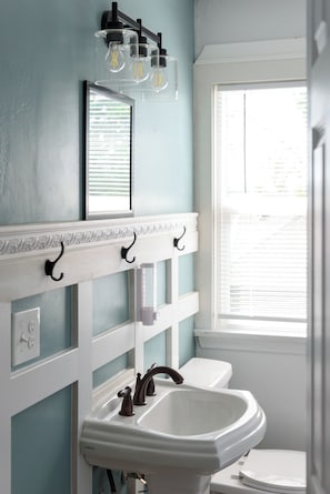 Une salle de bain avec un lavabo blanc, un miroir et une fenêtre avec des stores.
