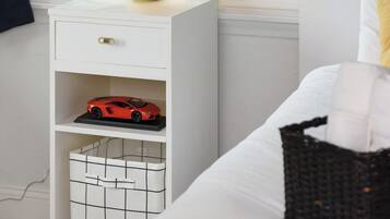 Un dormitorio con cama, una mesita de noche con lámpara, una estantería con un coche de juguete y una ventana con cortinas.
