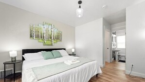 Un dormitorio moderno con una cama grande, dos mesitas de noche, una lámpara de pared y un baño visible.