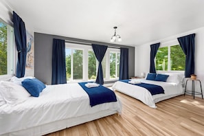Une chambre d’hôtel avec deux lits, de grandes fenêtres, un luminaire au plafond et une petite table.